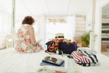 Woman unpacking suitcase in beach house bedroom - HOXF04568