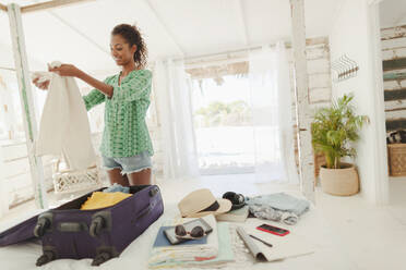 Young woman unpacking suitcase on beach hut bed - HOXF04576