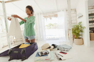 Junge Frau beim Auspacken des Koffers auf dem Bett einer Strandhütte - HOXF04576