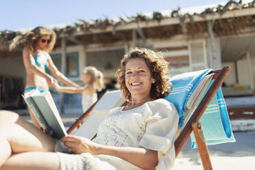 Portrait happy woman reading book, relaxing on sunny beach - HOXF04586