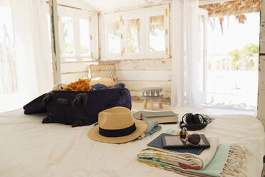 Suitcase, sun hat, sunglasses, book and digital tablet on beach house bed - HOXF04595