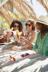 Mutter und erwachsene Töchter trinken Cocktails in einer sonnigen Strandbar - HOXF04598
