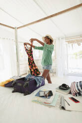 Glückliche Frau beim Auspacken des Koffers im Schlafzimmer des Strandhauses - HOXF04599