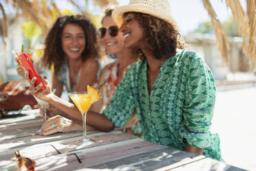 Glückliche Frauen, die ihr Smartphone benutzen und Cocktails an einer sonnigen Strandbar trinken - HOXF04602