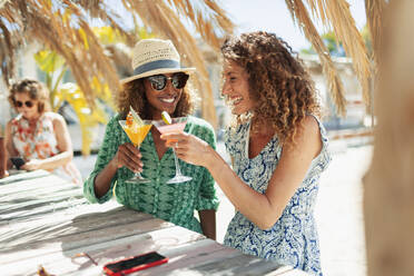 Glückliche junge Freundinnen trinken Cocktails an einer sonnigen Strandbar - HOXF04612