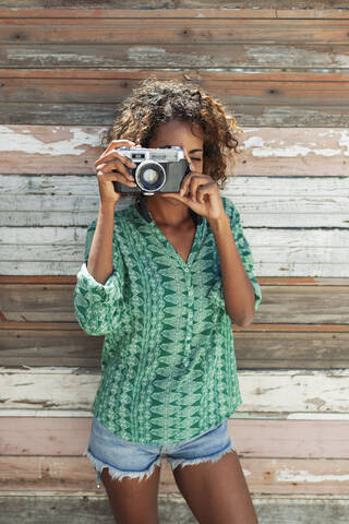 Porträt einer jungen Frau mit einer Retro-Kamera vor einer Holzbohlenwand, lizenzfreies Stockfoto