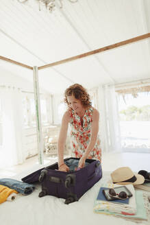 Frau beim Auspacken des Koffers im Schlafzimmer einer Strandhütte - HOXF04620