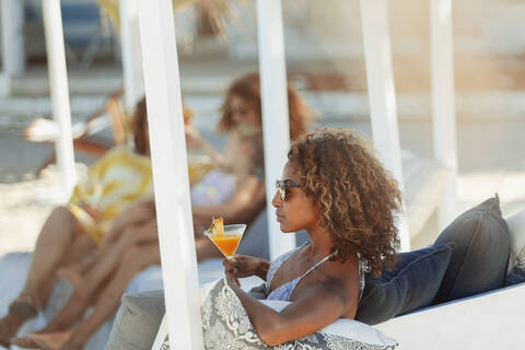 Junge Frau entspannt sich mit einem Cocktail auf einer Strandterrasse, lizenzfreies Stockfoto
