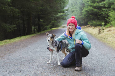 Portrait woman hiking with dog in woods - HOXF04646