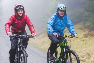 Vater und Sohn beim Mountainbiken im Regen - HOXF04746