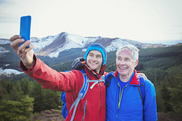 Vater und Sohn machen ein Selfie mit Bergen im Hintergrund - HOXF04752