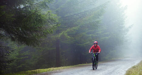 Man mountain biking in rain - HOXF04755