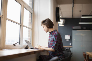 Geschäftsfrau arbeitet am digitalen Tablet im Bürofenster - HOXF04808
