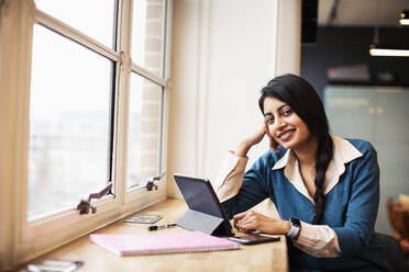 Porträt einer selbstbewussten, lächelnden Geschäftsfrau, die ein digitales Tablet im Fenster benutzt - HOXF04830