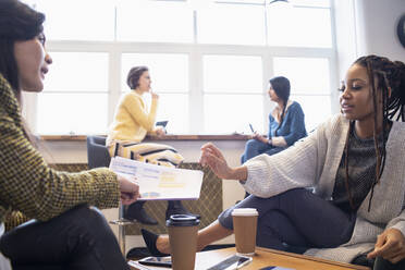 Businesswomen discussing paperwork in office - HOXF04838