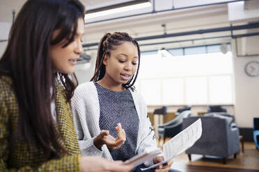 Businesswomen discussing paperwork in office - HOXF04859