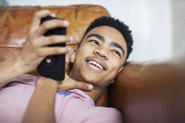 Lächelnder Jugendlicher mit Smartphone auf dem Sofa - HOXF04865