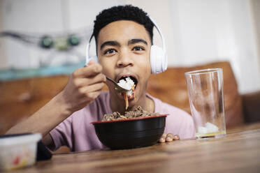 Porträt eines Teenagers mit Kopfhörern, der am Kaffeetisch isst - HOXF04866