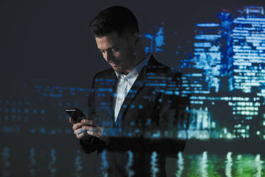 Doppelbelichtung Geschäftsmann mit Smartphone gegen Hochhauslichter bei Nacht - CAIF23393