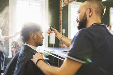 Männlicher Friseur sprüht die Haare eines Mannes im Friseursalon - CAIF23423