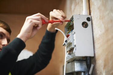 Männlicher Elektriker mit Schraubenzieher bei der Arbeit an einer elektrischen Schalttafel - CAIF23455