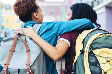 Affectionate young women friends with backpacks hugging - CAIF23513
