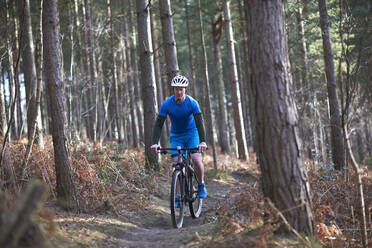 Mann beim Mountainbiken auf einem Weg im Herbstwald - CAIF23528