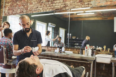 Männlicher Friseur, der sich darauf vorbereitet, das Gesicht eines Kunden im Friseursalon zu rasieren - CAIF23538