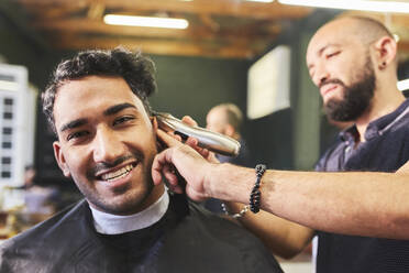 Porträt eines lächelnden jungen Mannes, der beim Friseur einen Haarschnitt erhält - CAIF23539