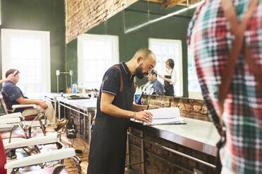 Männlicher Friseur mit Blick auf den Zeitplan im Friseursalon - CAIF23541