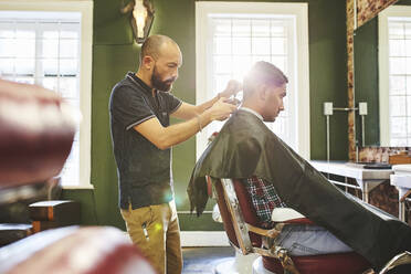 Fokussierter männlicher Friseur, der einem Kunden im Friseursalon die Haare schneidet - CAIF23544