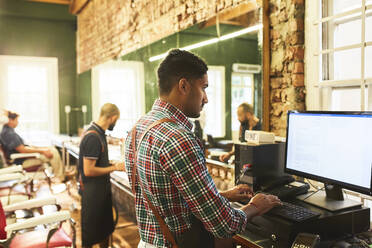 Männlicher Friseur, der einen Computer im Friseursalon benutzt - CAIF23545