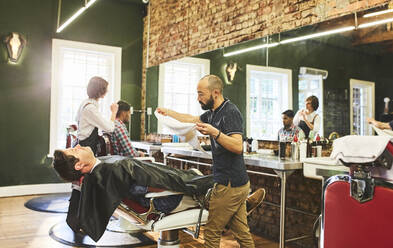 Männlicher Friseur bereitet sich darauf vor, das Gesicht eines Kunden vor der Rasur zu bedampfen - CAIF23552