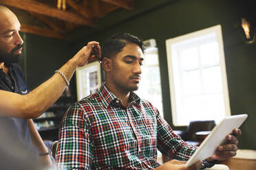 Man using digital tablet while receiving haircut in barbershop - CAIF23553