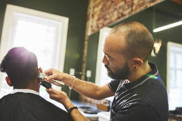 Männlicher Friseur mit Trimmern beim Haarschnitt eines Kunden in einem Friseursalon - CAIF23557