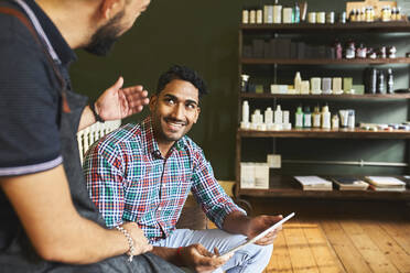 Männlicher Friseur und Kunde mit digitalem Tablet im Gespräch im Friseursalon - CAIF23560