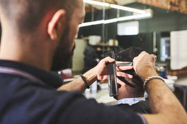 Männlicher Friseur schneidet einem Kunden die Haare im Friseursalon - CAIF23576