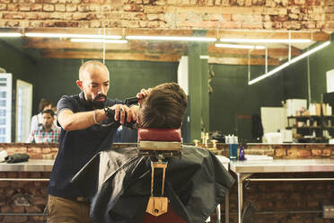 Männlicher Friseur schneidet einem Kunden die Haare im Friseursalon - CAIF23584