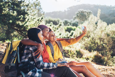 Glückliche Mutter und Töchter machen ein Selfie, wandern im sonnigen Wald - CAIF23589