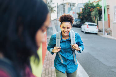 Laughing, happy young woman with backpack on sidewalk - CAIF23604