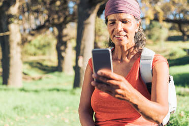 Wanderin benutzt Smartphone im sonnigen Wald - CAIF23608