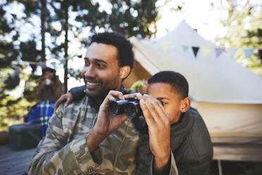 Curious father and son with binoculars at campsite - CAIF23622