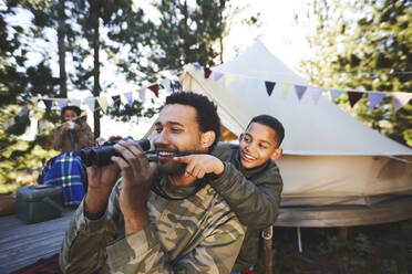 Happy, curious father and son with binoculars at campsite - CAIF23625