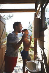Vater und Sohn beim Zähneputzen auf dem sonnigen Campingplatz im Badezimmerspiegel - CAIF23627