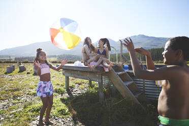 Verspieltes lesbisches Paar und Kinder mit Strandball an einem abgelegenen, sonnigen Sommerpool - CAIF23635