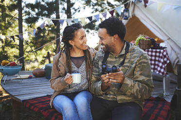 Verliebtes junges Paar mit Fernglas beim Kaffeetrinken auf dem Campingplatz - CAIF23636