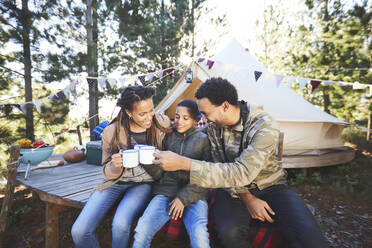 Glückliche Familie trinkt Kaffee und heiße Schokolade auf einem Campingplatz im Wald - CAIF23641