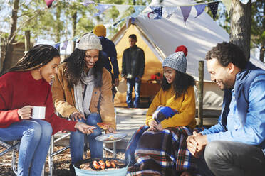 Glückliche Freunde und Familie beim Kochen am Lagerfeuer auf dem Campingplatz - CAIF23650