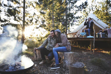 Glückliches Paar am Lagerfeuer auf dem Campingplatz im Wald - CAIF23655