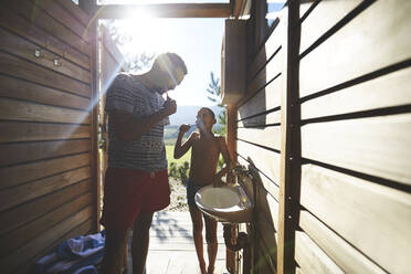 Vater und Sohn putzen sich die Zähne im sonnigen Badezimmer des Campingplatzes - CAIF23656